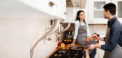 Cooking Together. Happy couple preparing dinner, frying on pan, looking at each other, girl sitting on countertop photo