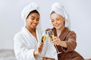 Relaxed girlfriends with eye patches on toasting with champagne while having skincare procedures at home photo