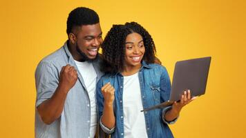 Smiling African American Couple Watching Sports On Laptop Together And Cheering, Standing Over Yellow Background With Copy Space photo