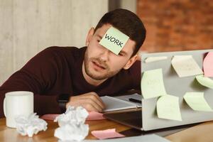 Overworked man having a nap sleeping at laptop with sticky notes everywhere, tired of office multitasking work indoor. Selective Focus photo