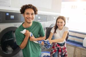 Two young adults are having a great time at the laundromat. One holds laundry while the other playfully interacts, creating a lively atmosphere in a modern laundromat. photo