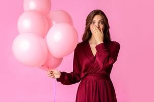 Forgot to take present. Surprised young lady holding air balloons and covering mouth with hand in shock, posing over colorful background with free space photo