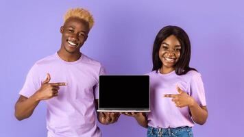 Millennial African American lady and guy pointing at empty laptop screen on lilac background, space for your website design. Panorama photo