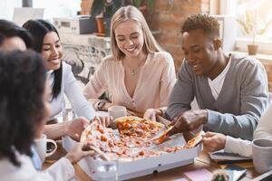 Happy multiracial colleagues eating pizza in office, having break while business meeting photo