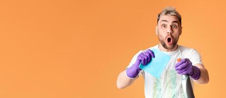 Surprised Young man is cleaning, Holding spray and bast in hands. Isolated on yellow background photo