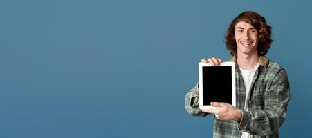Smiling teenage guy showing tablet computer with empty screen on turquoise background, space for design photo