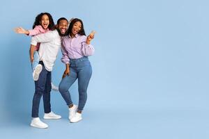 Spending Time With Family Is Fun. Full body length of excited African American man, woman and girl laughing and posing isolated over yellow studio wall. Cheerful father carrying his daughter on back photo