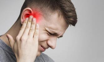 Young man has sore ear, suffering from otitis, touching his inflamed head, close up, empty space photo
