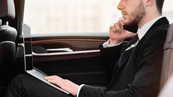 Always In Touch. Confident chief executive in suit using personal computer and making phone call in taxi, copy space, side view photo