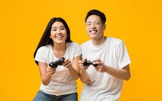 Gambling happy asian couple playing game with joysticks, yellow studio background photo