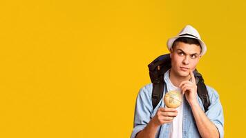 Dont't know where to go. Thoughtful traveler with big backpack and globe over yellow studio background, panorama with free space photo