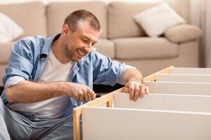 Smiling Man Assembling Furniture Installing Cabinet After Relocation Sitting At Home. Selective Focus, Free Space photo