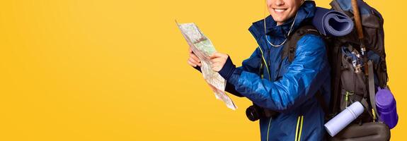Happy man backpacker following map, smiling over orange background, side view photo