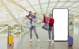 Four friends enjoy their time at the airport, smiling and jumping near their colorful luggage while posing with a large blank backdrop for photos, creating a lively atmosphere. photo