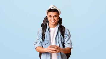 Smiling hiker man sending message with mobile phone over orange studio background, panorama, copy space photo