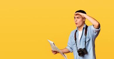 Shocked traveler with map and camera looking at empty space over orange background, panorama photo