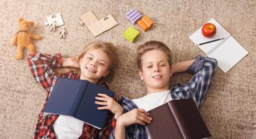 Siblings Brother And Sister Doing Homework Together Lying On Floor Having Fun Posing With Books At Home. Top View photo