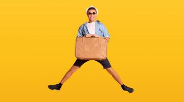 Happy guy tourist jumping with suitcase over orange background, panorama photo