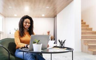 Portrait of smiling woman sitting at desk, using laptop and writing in notebook, taking notes, watching tutorial, lecture or webinar, studying online at home looking at screen, free copy space photo