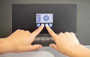 A person hands are seen adjusting the temperature settings on a sleek digital display panel in a kitchen. The display shows a temperature of 17 degrees, indicating precise control. photo