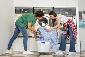 A young couple is enjoying their time at a laundromat, happily loading a washing machine with clothes while sharing a moment of teamwork and laughter in a vibrant, clean environment. photo