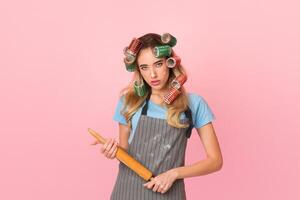 Angry housewife doing routine annoying homework in apron with spots of flour and rolling pin in hands photo