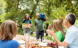 A group of friends gathers in a lush garden, sharing laughter while one person carries fresh vegetables and another holds a cooler. The atmosphere is joyful and inviting, filled with nature. photo