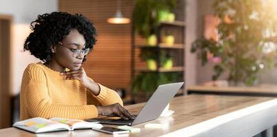Black girl working in cafe, browsing on laptop and taking notes, empty space photo