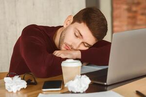 Exhausted Man Sleeping At Laptop Tired Of Multitasking And Overworking Sitting In Office. Selective Focus photo