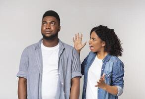 Angry black lady screaming at her annoyed boyfriend, shouting with fury and emotionally gesturing, light background with free space photo