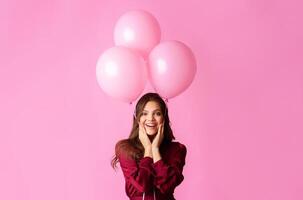 Playful Mood. Cheerful Young Lady Holding Three Rosy Balloons And Touching Cheeks In Excitement, Posing Over Colorful Background photo