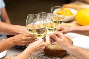 Friends gather around a table, clinking glasses filled with white wine in celebration. The atmosphere is warm and inviting, with food and laughter shared among the group. photo