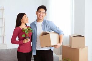 Moving And Repair Concept. Loving chinese couple enjoying new apartment and keep the box and green plant in hands photo