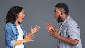 Couple Arguing. Angry Black Man And Woman Shouting At Each Other, Standing On Light Background In Studio, Side View photo