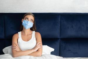 Self-Isolation. Depressed Girl In Protective Mask Sitting In Bed Bored From Quarantine Lifestyle And Loneliness photo