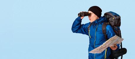 Hiker with map through binoculars at free space, orange studio background, panorama photo