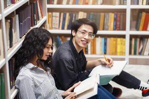 Studying Together. Two multiracial students doing homework, sitting on the floor in modern library, copyspace photo