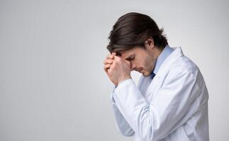Profile portrait of depressed overworked male doctor holding stethoscope in hands, having headache, desperate and powerless, panorama with free space photo