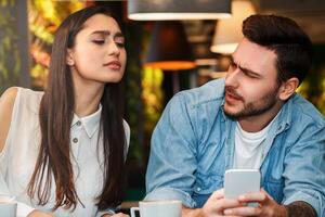Jealous Girlfriend Reading Boyfriend's Messages While He Texting On Phone Suspecting Infidelity Sitting In Cafe. Private Space In Relationship photo