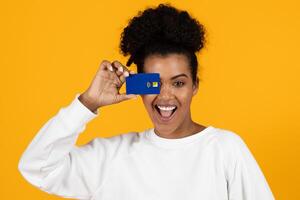 A joyful woman smiles widely while holding a blue card in front of her face. The bright yellow backdrop enhances her cheerful expression and creates an energetic atmosphere. photo