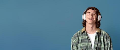 Portrait of cool teenager in headset relaxing to his favorite music on turquoise background photo