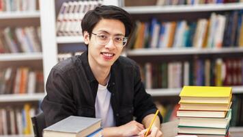 Confident Student. Cheerful asian guy sitting at library, taking notes, doing research, looking at camera, copyspace photo
