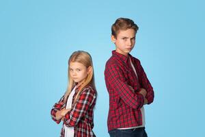 Siblings Conflicts. Offended Brother And Sister Standing Back To Back Not Talking To Each Other After Quarrel, Blue Studio Background With Copy Space photo