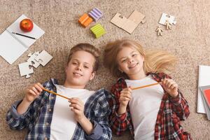 Homework Time. Siblings Lying On Floor Holding Pencils Looking At Camera Posing At Home. Top View photo