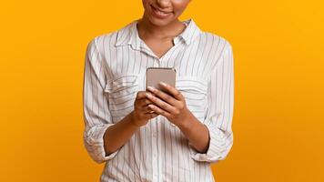 Modern Smartphone In Hands Of Unrecognizable African American Girl Standing On Yellow Background In Studio, Panorama With Empty Space photo