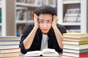 Studying Too Much. Tired asian student in specs grabbing his head, preparing for exams, trying to focus, copyspace photo