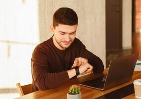 Working Hours. Office Worker Guy At Laptop Checking Time Sitting At Work Desk In Modern Office. Selective Focus photo