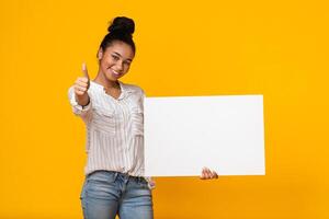 My Recommendation. Black Girl Holding Blank Placard With Free Space For Your Ad And Showing Thumb Up, Recommending Something, Yellow Background photo