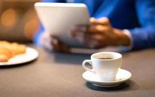 Coffee Break. Unrecognizable afro guy using tablet computer at cafe and drinking coffee, focus on cup, copyspace photo