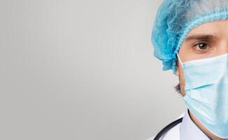 On Guard Of Coronavirus. Half Face Portrait Of Confident Male Doctor In Medical Mask And Hair Net Looking At Camera, Panorama With Free Space photo